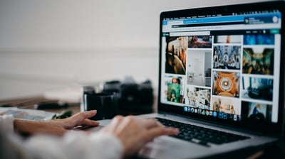 a person is typing in his laptop which displays some contents and posters