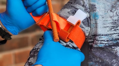 C.A.T. 7, tourniquet being applied to arm during training using two hands wearing blue nitrile glove