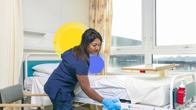 a nurse in scrubs and gloves cleaning a patient's bed