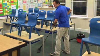 a man cleaning a classroom classroom with a vacuum