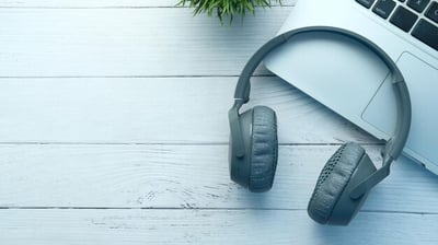 a laptop and headphones on a desk with a plant in the background, working on a transcription