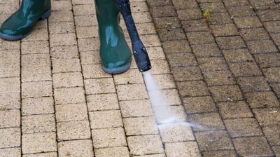 Man using a power washer on a surface, demonstrating before & after, with a visibly clean area.