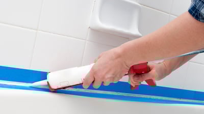 Professional applying caulk to seal the edges of a shower, ensuring a waterproof barrier.