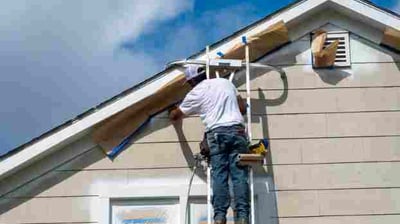 a man on a ladder painting a house with a sprayer