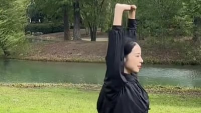 a woman in a black jacket and jeans standing in a park