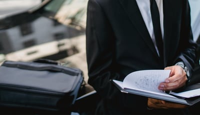 Un professionnel assis sur le capot d’une voiture, en train de prendre des notes sur un carnet.