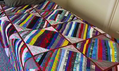 A twin-sized bed with a grey striped quilt featuring multicolored accent stripes, a gift for son