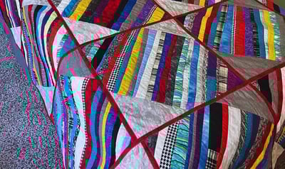 colorful quilt with red sashes and multicolored strips made for my son