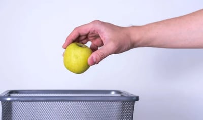 Hand tossing spoiled apple into trash can