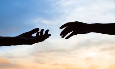 two hands reaching out to each other in front of a sunset