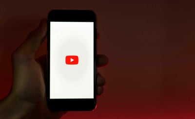 Hand holding a phone displaying the YouTube logo on a dark background