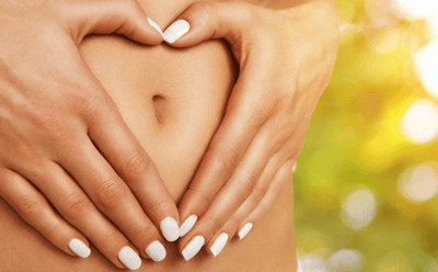 a woman's hands making a heart shape with her hands on her stomach with beautiful skin