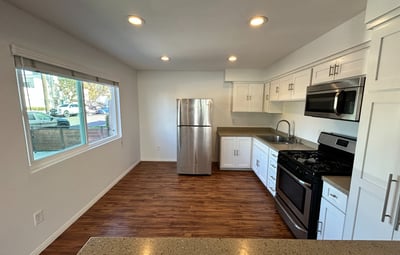 A modern kitchen with white cabinetry, black countertops, and stainless steel appliances