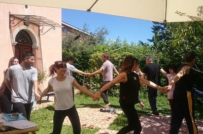 a group of people holding hands and dancing in a garden, classe di bioenergetica