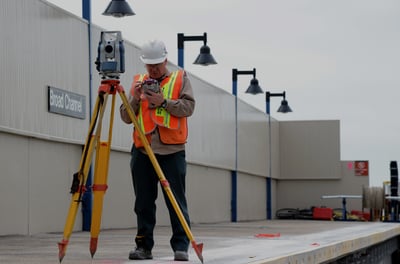 a man in a hard hat and safety vest using a tripod