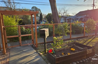 a hogwire garden fence and gate with landscaping planters