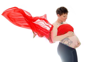 Photo de grossesse avec un voile volant rouge et la future mère tenant son ventre