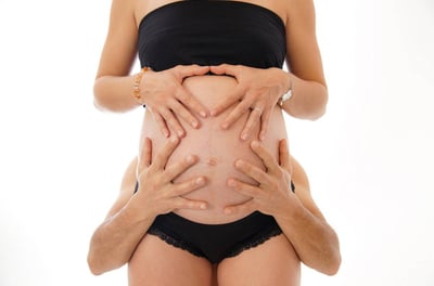 Photo de grossesse avec les mains des futurs parents posées sur le ventre bien rond