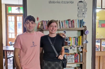 One student and one teacher standing in front of a bookshelf with a quote about travel and reading o