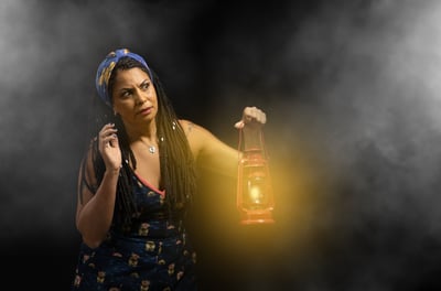 Uma mulher segurando uma lamparina, com ar de suspense e curiosidade, num fundo escuro e com fumaça