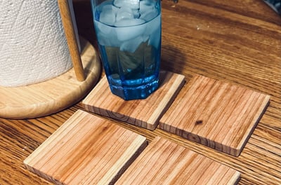 a glass of water on a square wooden cedar coaster sitting on a table