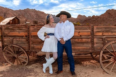 a man and woman in cowboy attire standing in front of a wagon