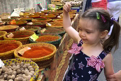 a little girl is standing in front of a table with a variety of spices