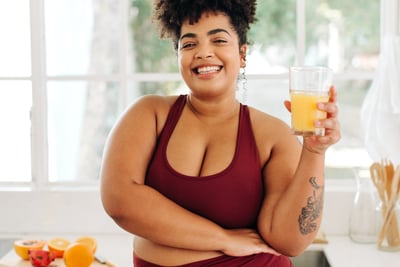 a woman in a red top and yoga pants is holding a glass of orange juice