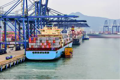 Container ship docking at sea port with cargo cranes and containers in background.