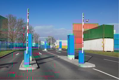 Automated gate system at sea port with barriers and container yard in background.