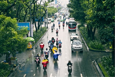 Urban road with motorbikes and cars in rainy conditions managed by smart traffic control systems.