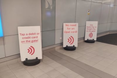 Three white signs stand on a tiled floor in what appears to be the Sydney Airport.