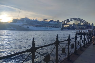 A large cruise ship is sailing on the water with the Sydney Harbour Bridge visible in the background.