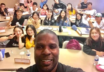 Dr. Marlon Ware standing in front of his class with students holding up the peace sign