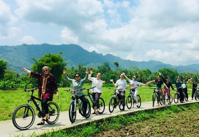 Wisatawan bersepeda santai menyusuri jalan pedesaan dengan pemandangan sawah dan Candi Borobudur di kejauhan