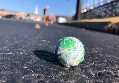 a small globe on the ground with students and school in the background