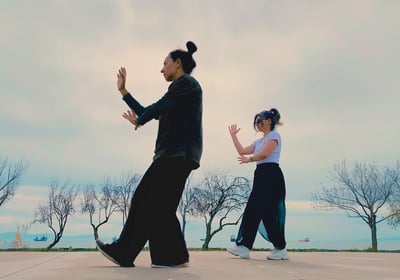 Ebru Tütek and student practicing Bagua walking by the sea, with bare trees and ships in the distance.