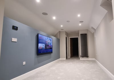 a large flat screen tv mounted on a wall with ceiling audio speakers. Brixton