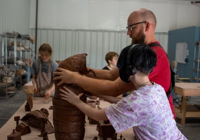 A teacher and middle school student holding a big clay creature up.