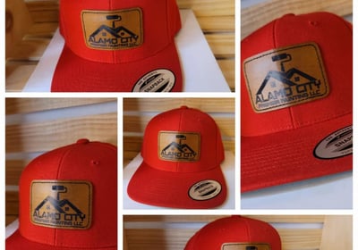 Red snapback hats with custom laser-engraved leather patches featuring Alamo City Painting LLC logo