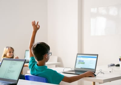Children raising hands and engaging in a tech learning environment with laptops