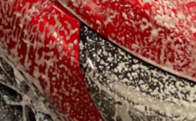 Une voiture rouge recouverte de mousse lors d'un nettoyage