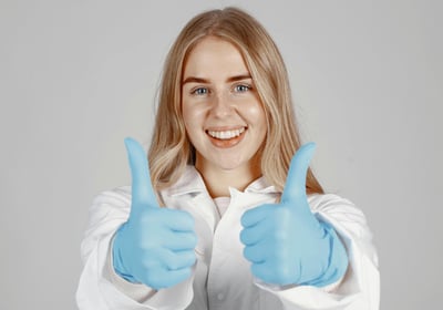 Female in lab coat with blue gloves giving thumbs up sign