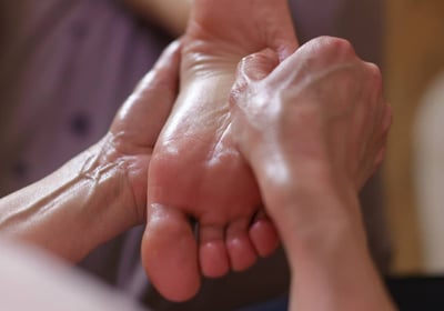 Mains massant un pied en douceur, symbole de soin ciblé et d’attention aux zones spécifiques.