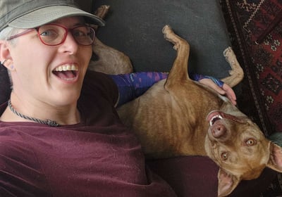A person and a brindle dog cuddle together on a couch while taking a selfie