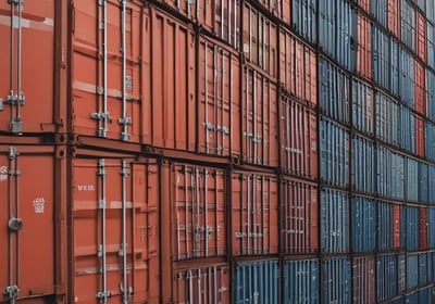 Stacks of bright orange shipping containers with the Hapag-Lloyd logo are arranged against a dark, overcast sky, creating a striking contrast. The containers are aligned neatly, showcasing international trade and logistics.