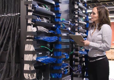 mulher em ambiente datacenter observando servidores e nobreaks