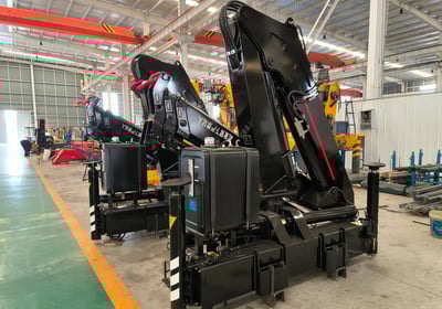 Factory floor view of several black SQZ132A.3 knuckle boom units, a type of crane machine, awaiting final