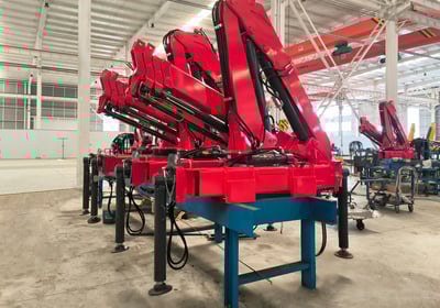 Production line: Red SQZ68B.3 (3.2T) articulating knuckle boom cranes on blue stands, pre-vehicle mounting.