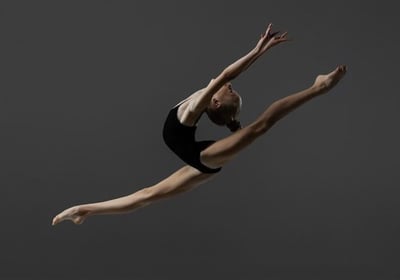 A young graceful rhythmic gymnast performing a split leap in the air.